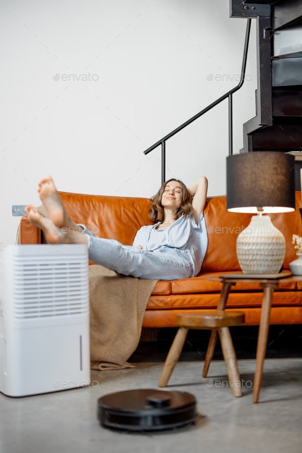 Woman sitting near air purifier and robotic vacuum cleaner
