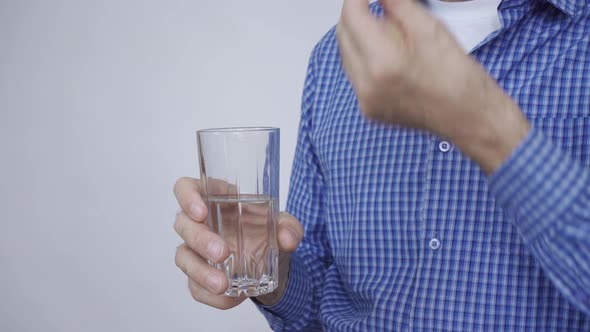 Closeup of a Man's Hands Holding a Glass of Water and a White Round Pill alt