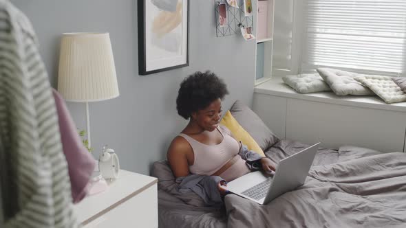 African American Woman Video Chatting on Laptop in Bed alt
