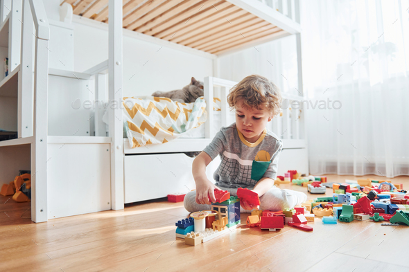 Cute little boy sitting and have fun indoors in the bedroom with plastic construction set