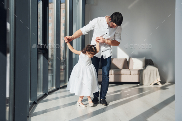 Happy father with his daughter in dress learning how to dance at home together