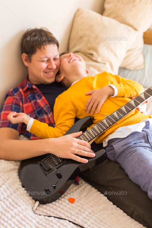 Millennial father and son playing, practicing electric guitar at home