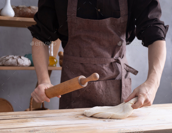 Baker man kneading or making dough with rolling pin and bakery ingredients for bread cooking