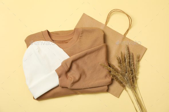 Sweatshirt, paper bag and beanie on beige background