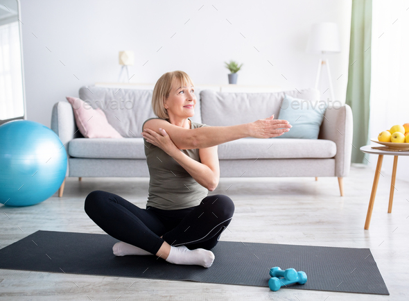 Sporty African American woman stretching her leg on yoga mat at home Stock  Photo by Prostock-studio