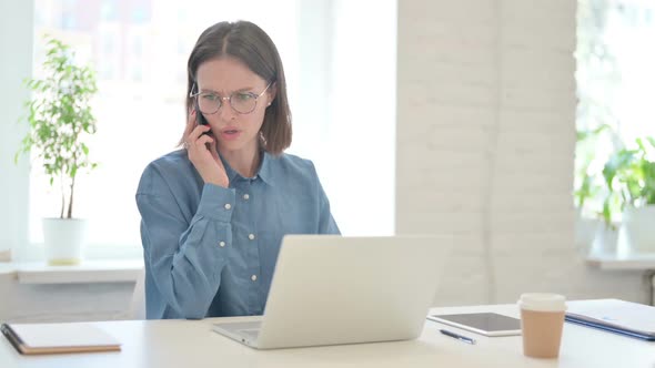 Angry Young Woman Working on Laptop and Talking on Phone alt