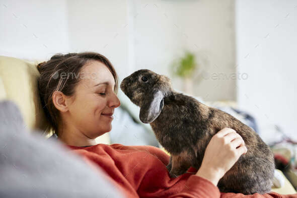 Pet house rabbit reaching towards woman with eyes closed on sofa