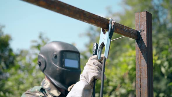 Builder Welds Metal Plank Fixed with Clamp To Fence Pole alt