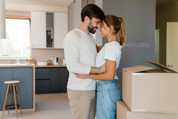 Beautiful couple hugging while standing by boxes in new apartment