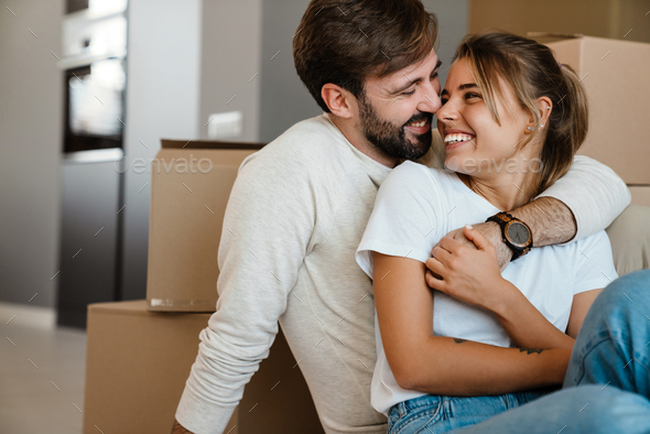 Beautiful couple hugging while sitting with boxes in new apartment