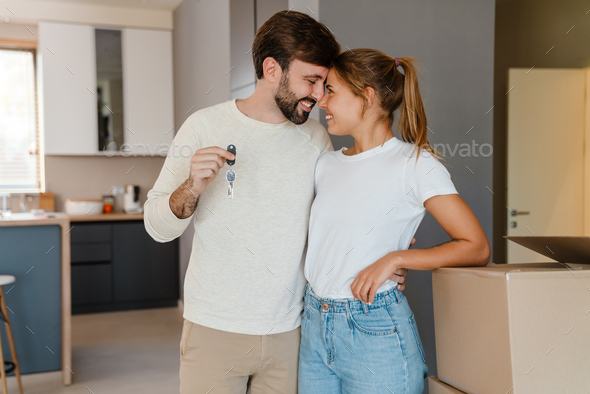 Beautiful couple smiling and holding key by boxes in new apartment