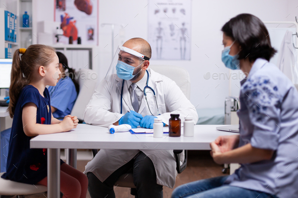 Medical doctor wearing face mask and visor writing prescription on clipboard