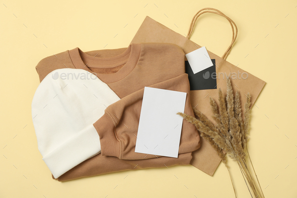 Sweatshirt, paper bag and beanie on beige background