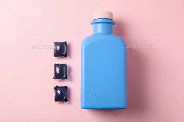 Laundry capsules and bottle of laundry liquid on pink background