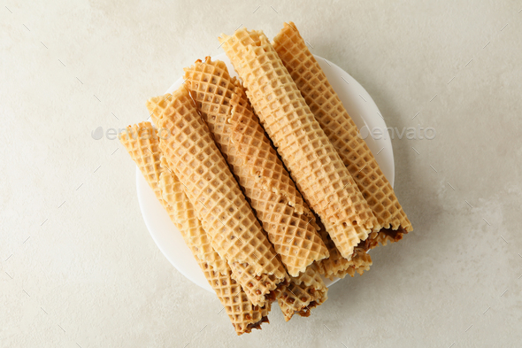 Plate with wafer rolls with condensed milk on white textured background