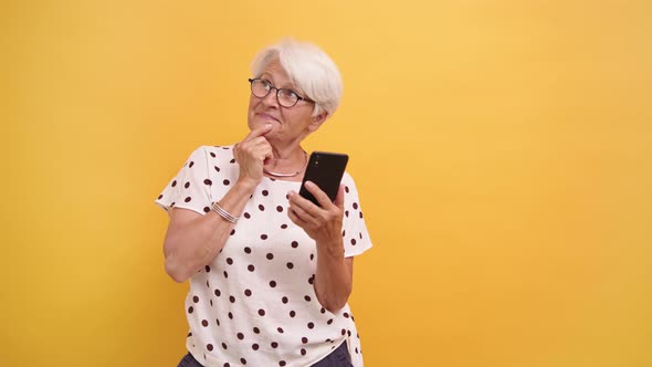 Senior Woman Holding Smartphone and Thinking About New Post for Social Media alt