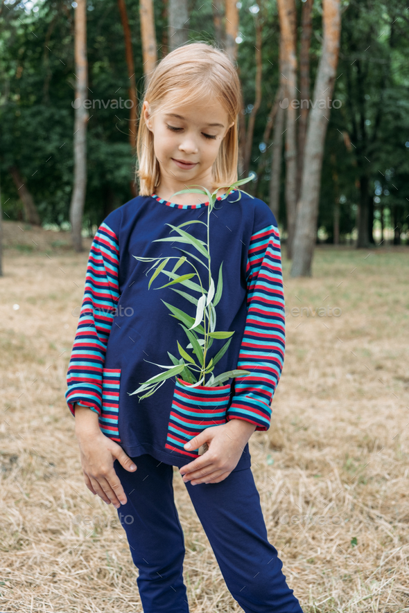 Environmental education for kids. Little girl holding young plant in hands against green tree