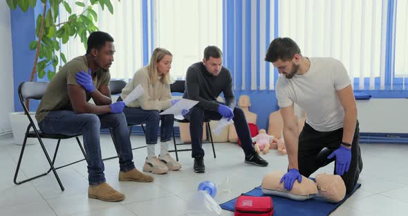 Man Instructor Showing How to Make Chest Compressions with Dummy During the First Aid Group Training alt