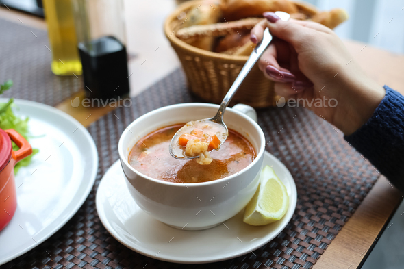 side view woman eating chicken soup in a cup with lemon and bread on the table