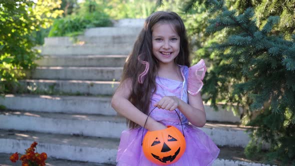 A Little White Girl in a Purple Witch Costume Throws Colorful Candy Wrappers From a Pumpkin