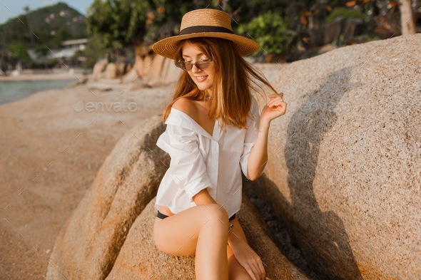 woman in bikini and white blouse with perfect figure posing on tropical beach.