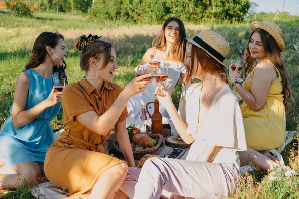 Friends having picnic in the countryside. Group of young women sitting on blanket in park near trees
