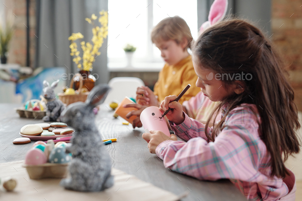 Cute little girl with highlighter drawing face of Easter rabbit on rolled paper - Stock Photo - Images