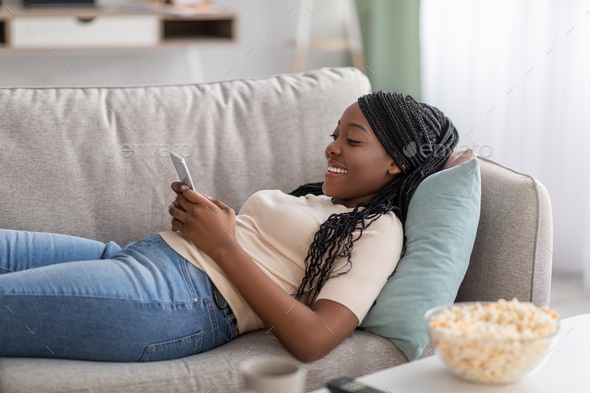 Happy black lady laying on couch with mobile phone