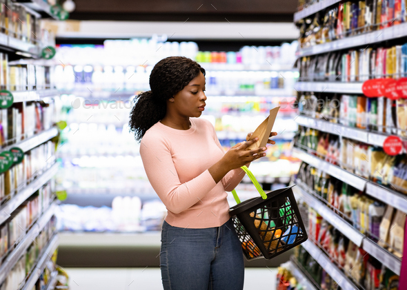 Beautiful African American woman making choice of products at supermarket