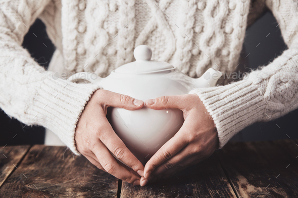 Adult woman hands hug big ceramic teapot