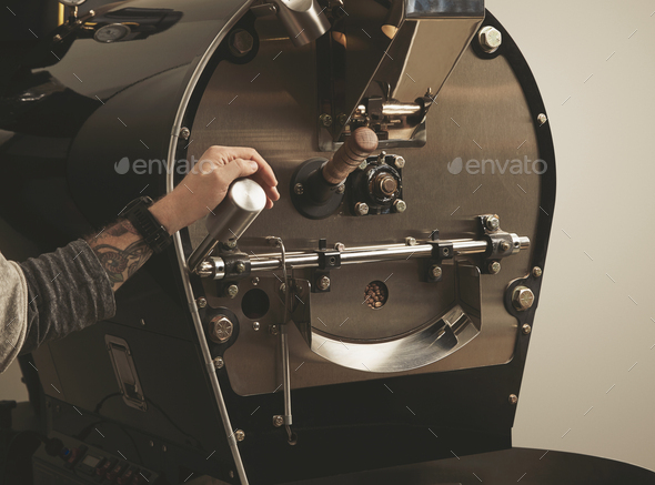Tattooed hand pulls lever in coffee roasting machine