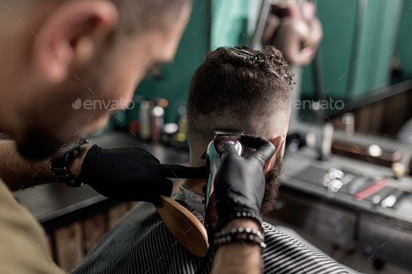 Barber in black gloves shaves man\'s hairs at the back at a barber shop
