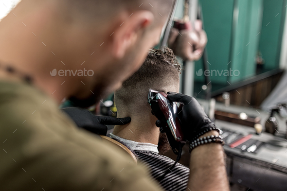 Barber in black gloves shaves man\'s hairs at the back at a barber shop