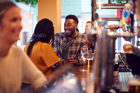Smiling Young Couple On Date Sitting At Counter Of Busy Bar