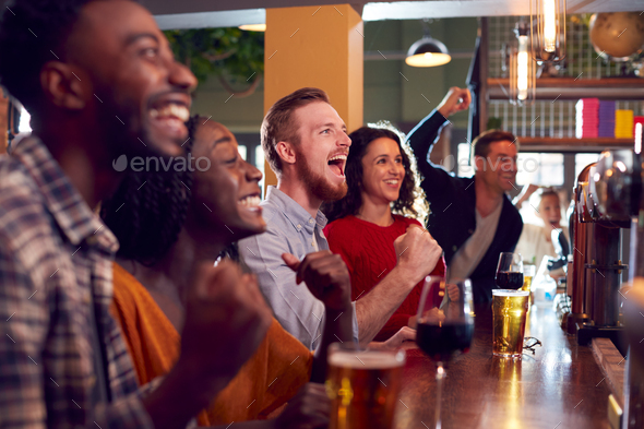 Group Of Excited Customers In Sports Bar Watching Sporting Event On Television