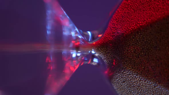 Glass Hourglass with Golden Sand on Purple Background alt