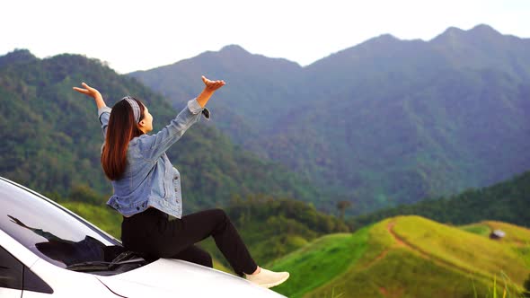 Young woman traveler sitting on a car watching a beautiful mountain view
