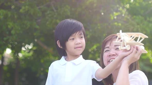Cute Asian Mother And Son Playing Wooden Airplane Together In The Park Outdoors alt