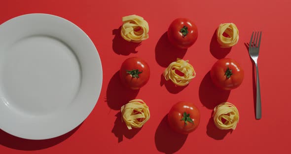 Video of fresh red tomatoes and pasta nests with plate and fork on red background alt