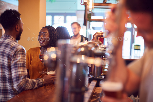 Smiling Young Couple On Date Sitting At Counter Of Busy Bar