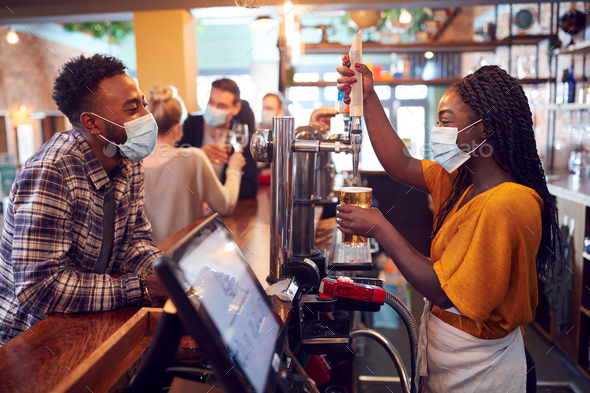 Female Bartender Wearing Face Mask Serving Male Customer With Beer During Health Pandemic