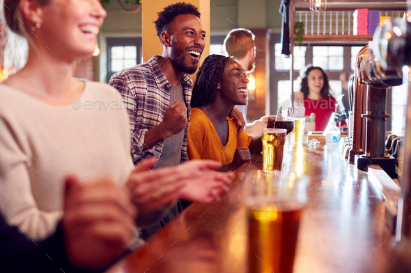 Group Of Excited Customers In Sports Bar Watching Sporting Event On Television