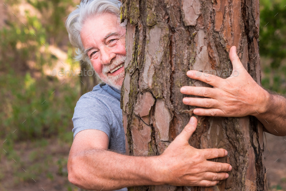 A senior adult man white hair hugging a tree in the wood - love for nature - earth\'s day concept.