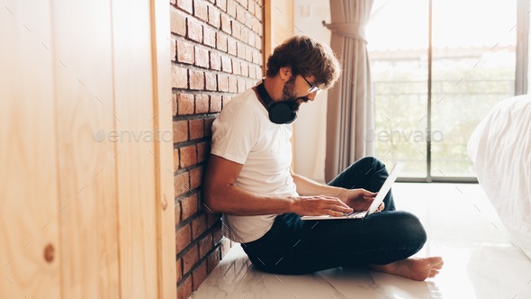Hipster man using laptop and sitting on floor at home.