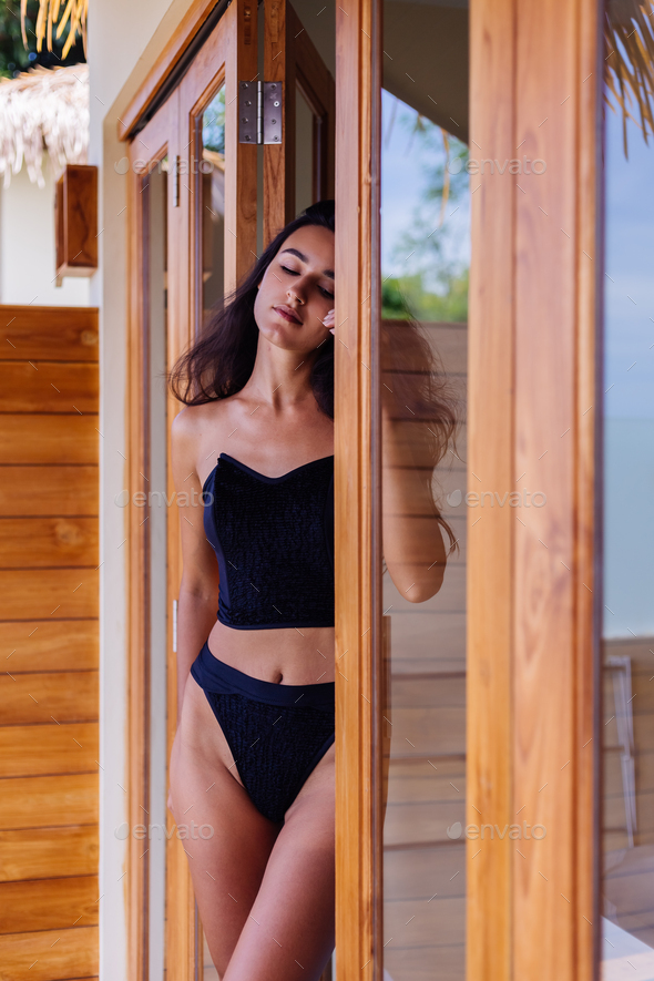 Caucasian fit tanned woman wearing vintage old bikini, posing at luxury hotel villa