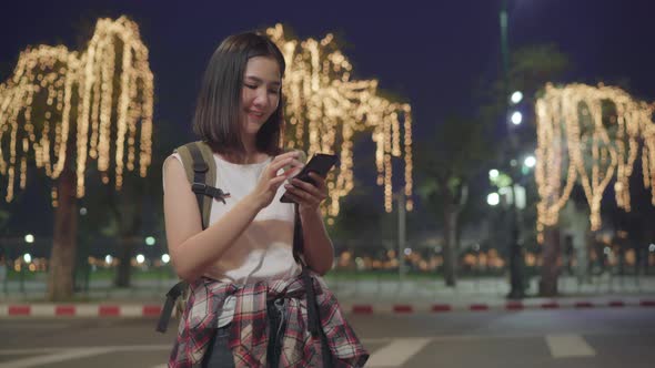 Asian tourist girl using mobile phone checking social media at night while walk along.