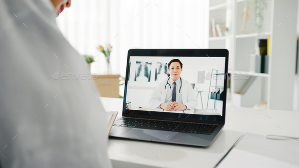 Young Asian lady doctor using laptop talking video conference call with doctor at desk in hospital.