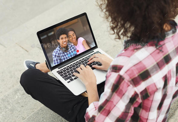 Young guy speaking to African American couple on webcam, using online video chat on laptop, outdoors