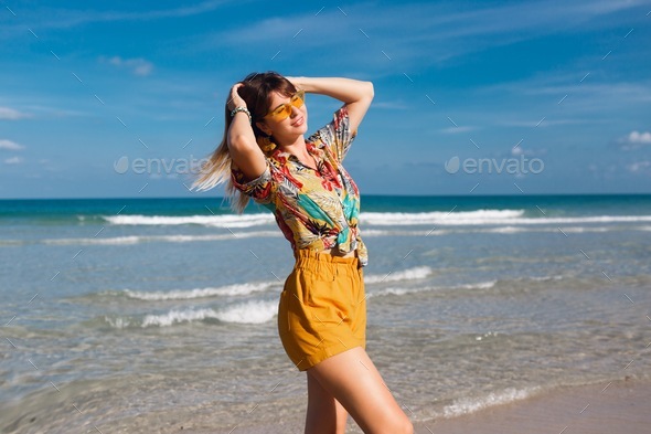 Happy woman in shirt with tropical print posing on the beach.