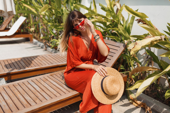 female in straw hat and orange playsuit resting on her villa during vacation on Bali.